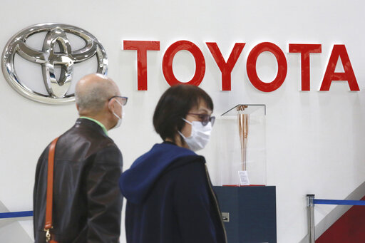 FILE - People walk past the logo of Toyota at a showroom in Tokyo, Monday, Oct. 18, 2021. Toyota is suspending production at all 28 lines of its 14 plants in Japan starting Tuesday, because of a “system malfunction” at a domestic supplier, the automaker said Monday, Feb. 28, 2022. (AP Photo/Koji Sasahara, File)