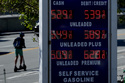 A person rides a scooter behind the gasoline price board of a gas station in San Francisco, Thursday, March 5, 2026. (AP Photo/Jeff Chiu)