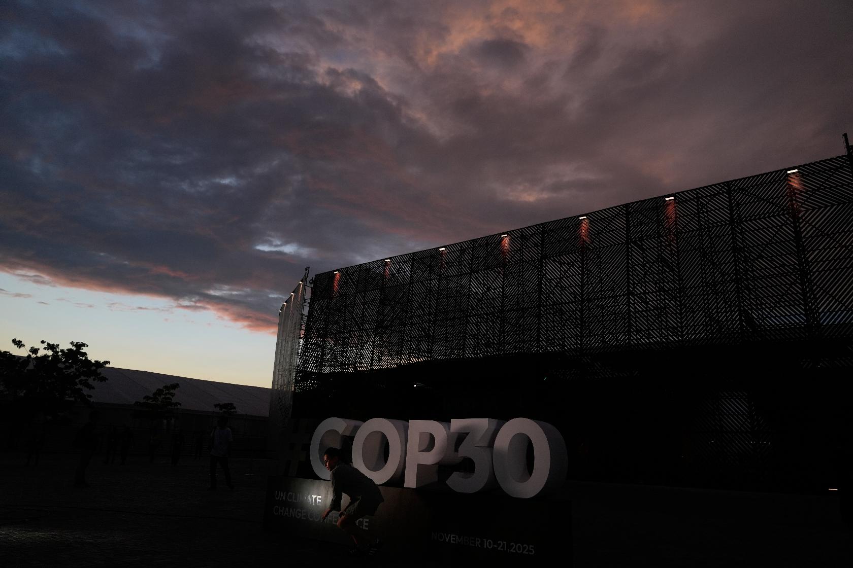 A person poses outside the venue for the COP30 U.N. Climate Summit as the sun sets on Saturday, Nov. 8, 2025, in Belem, Brazil. (AP Photo/Fernando Llano)