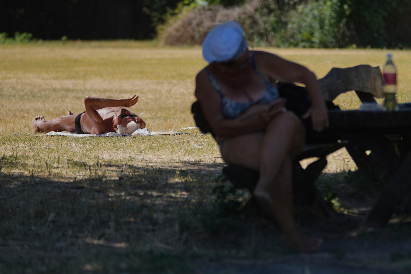 A person sits in the shade while another lies sunbathing during a hot summer day in Belgrade, Serbia, Thursday, July 3, 2025. (AP Photo/Darko Vojinovic)