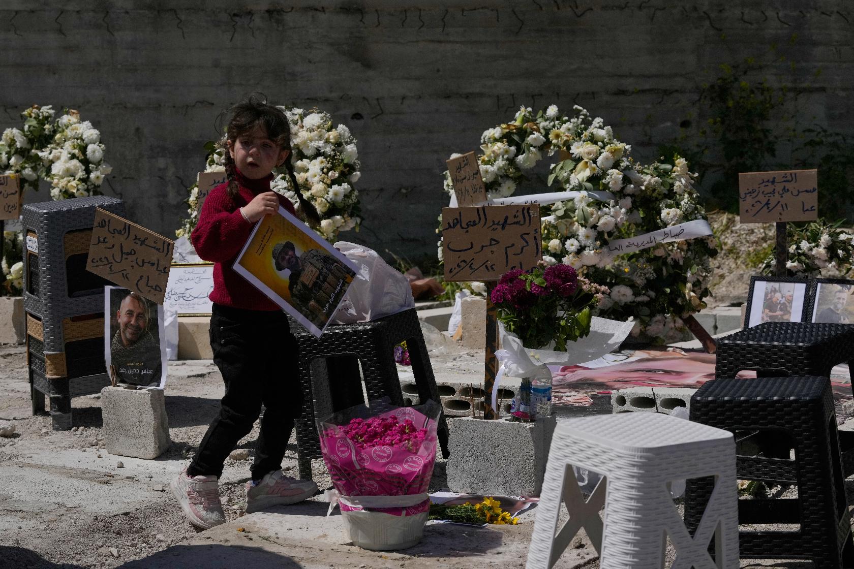 A young girl carries a portrait of a killed Hezbollah fighter at a mass grave where civilians and Hezbollah fighters killed in Israeli airstrikes are temporarily buried in the southern port city of Sidon, Lebanon, Tuesday, April 14, 2026. (AP Photo/Mohammed Zaatari)
