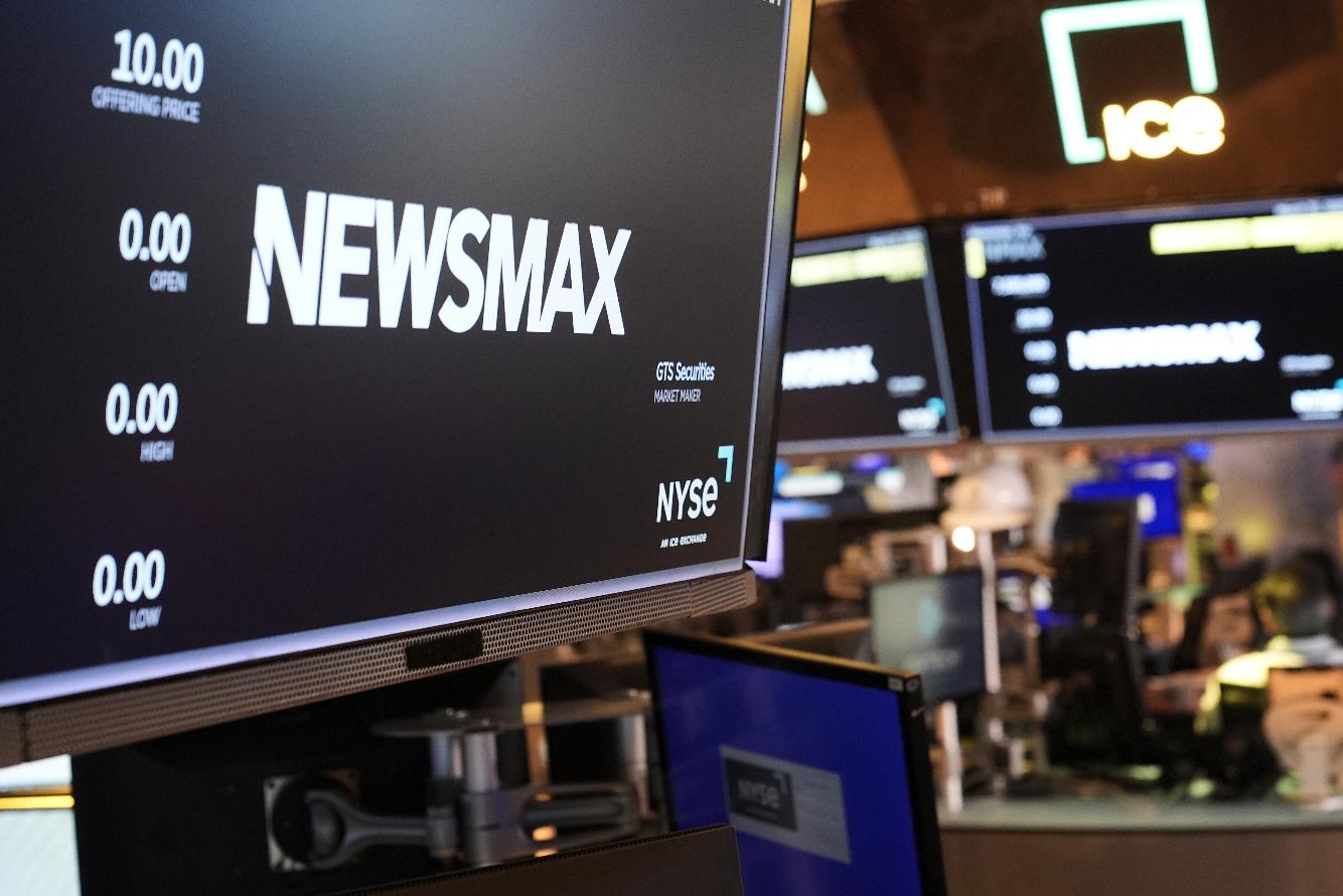 FILE - A display shows a Newsmax logo on the day of their IPO on the floor at the New York Stock Exchange in New York, March 31, 2025. (AP Photo/Seth Wenig, File)