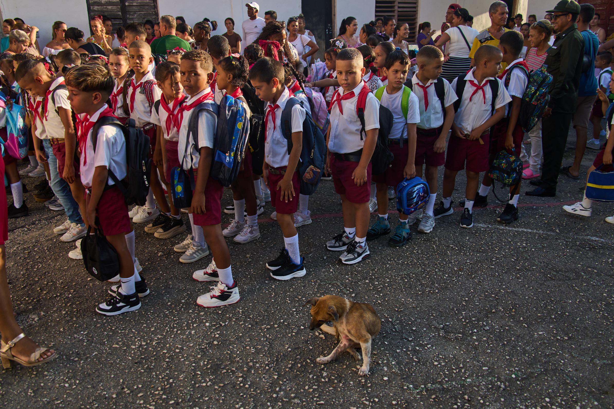 Children line up for their national anthem in the school courtyard where a stray dog sits by on the first day back to school in Minas, Cuba's Havana province, Tuesday, Sept. 1, 2026. (AP Photo/Ramon Espinosa)