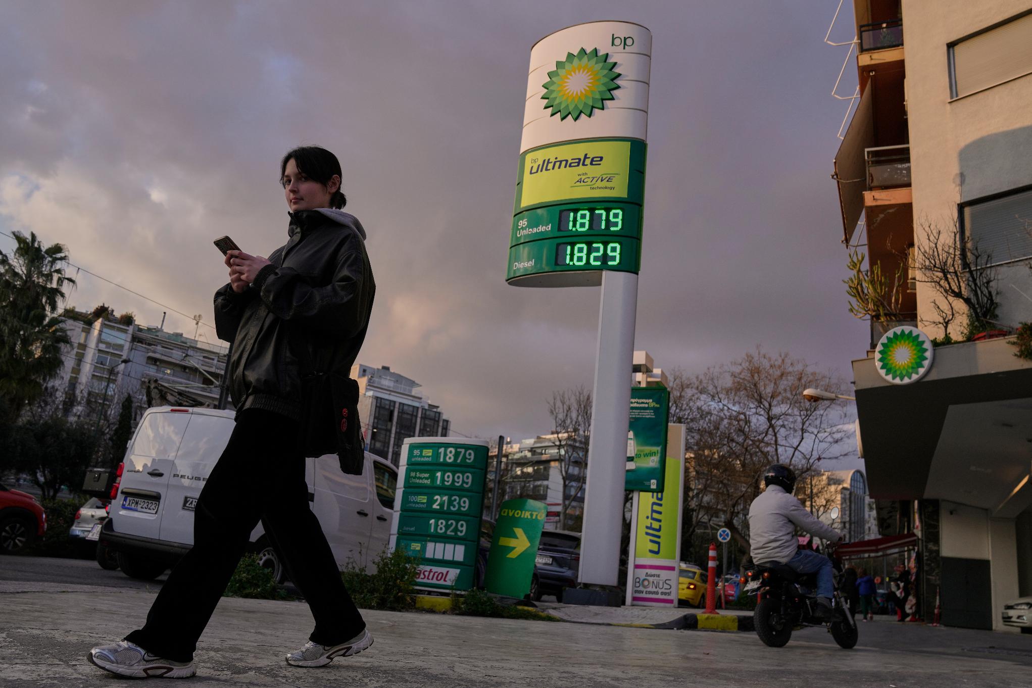 A woman walks past a sign showing current fuel prices stands outside a gas station in Athens, Greece, on Wednesday, March 11, 2026. (AP Photo/Petros Giannakouris)