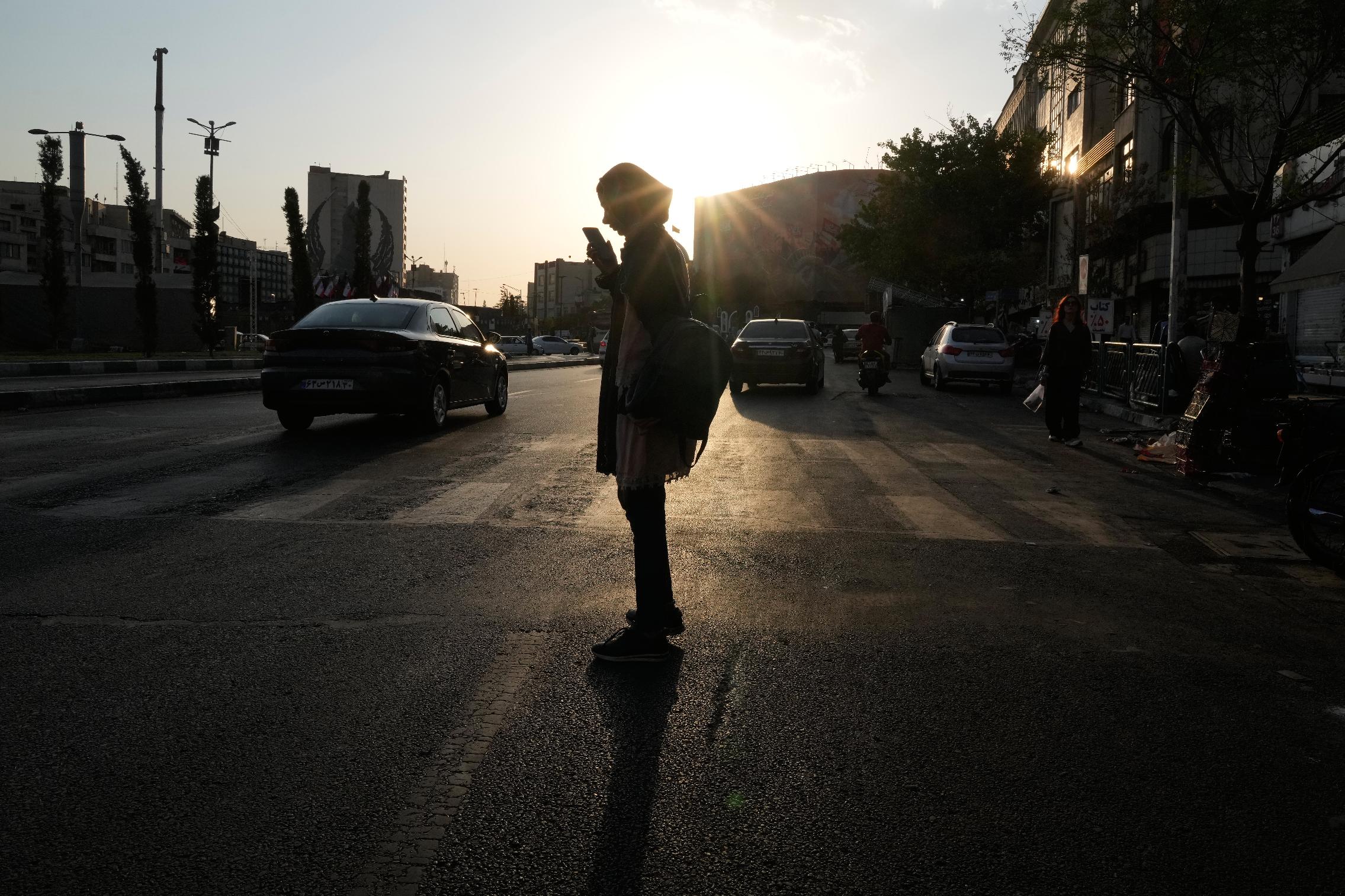 A woman is silhouetted against the sun as she checks her cellphone at Islamic Revolution square in downtown Tehran, Iran, Saturday, Aug. 15, 2026. (AP Photo/Vahid Salemi)