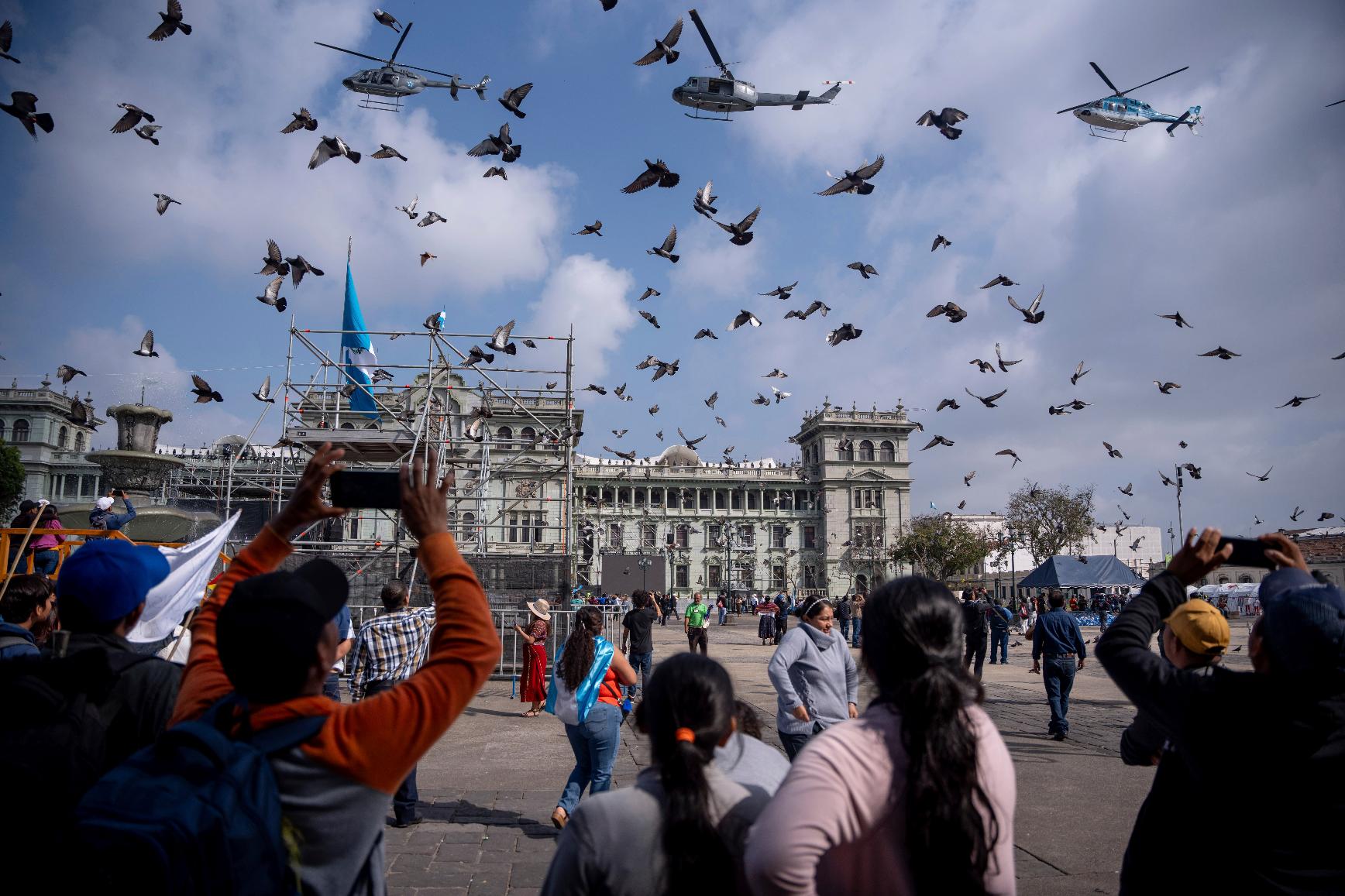 People watch helicopters fly in formation over Constitution Plaza before the inauguration of Guatemalan President-elect Bernardo Arévalo outside the National Palace in Guatemala City, Sunday, Jan. 14, 2024. (AP Photo/ Santiago Billy)