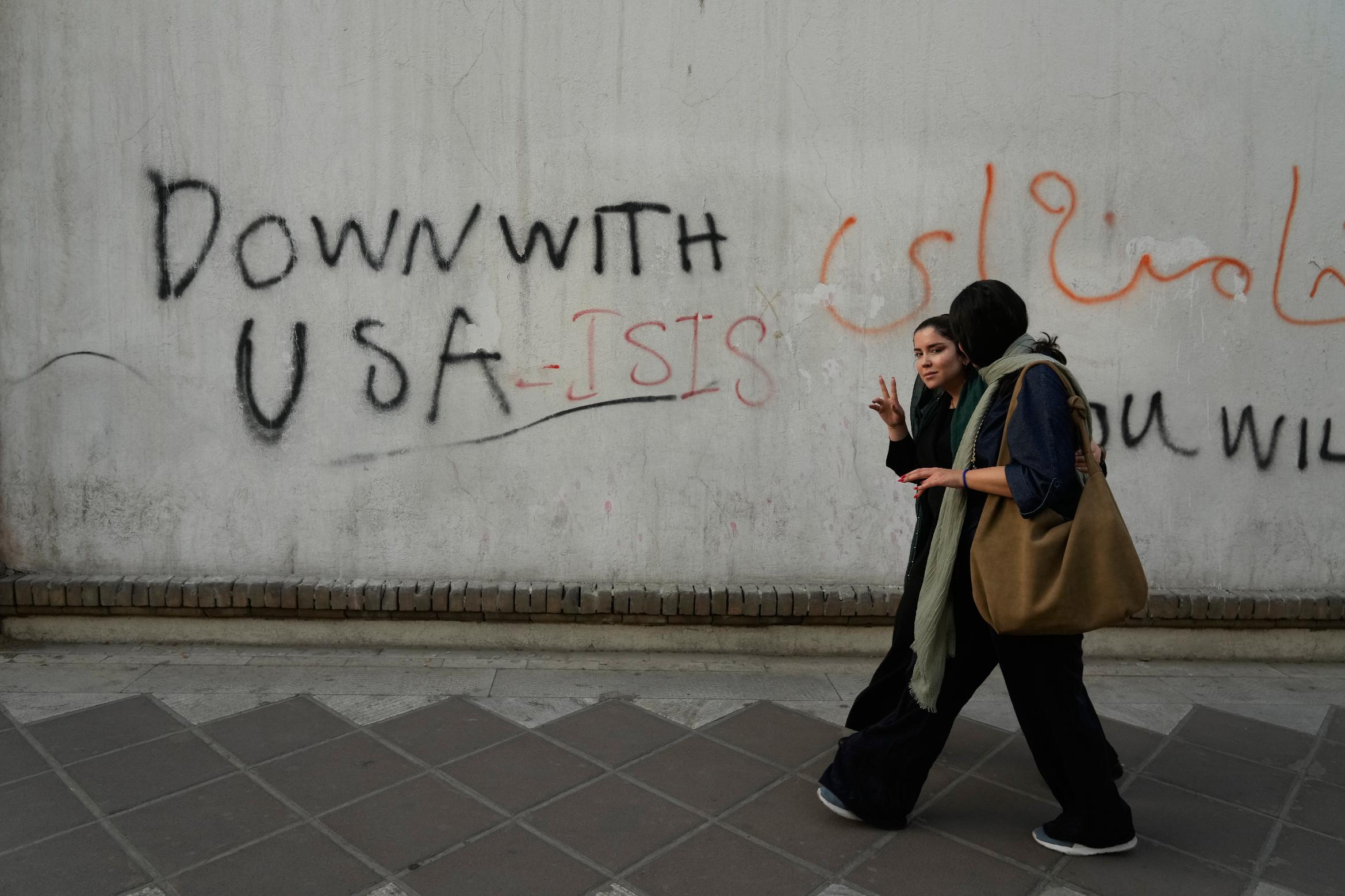 A woman reacts to the camera as she walks past an anti-U.S. graffiti painted on the wall of the British Embassy in Tehran, Iran, Saturday, June 6, 2026. (AP Photo/Vahid Salemi)
