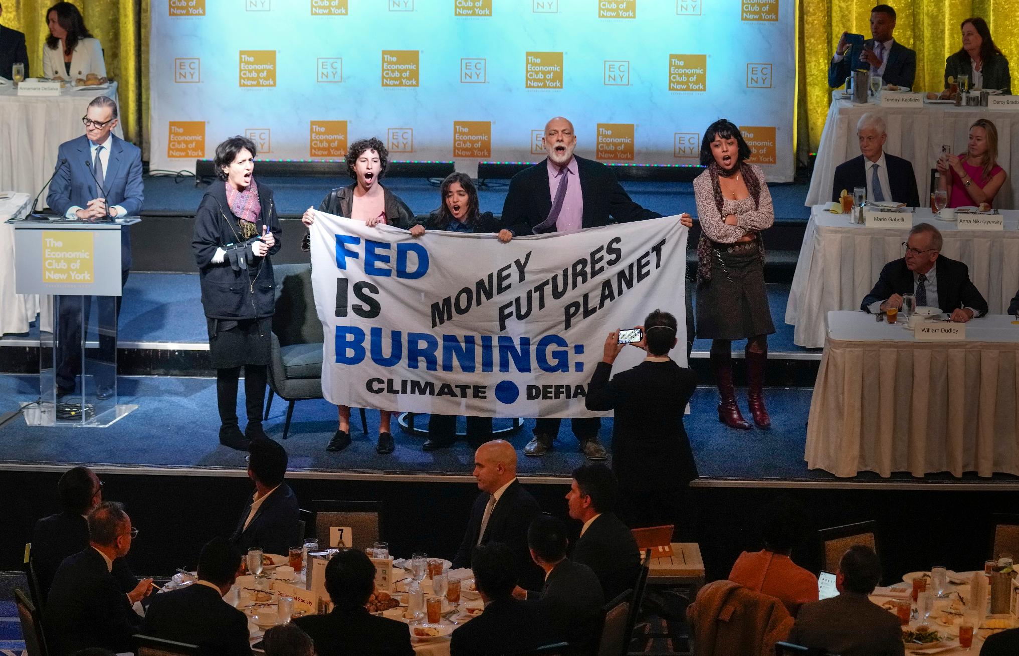 Climate activists step on stage with a banner before Federal Reserve Chairman Jerome Powell speaks at a meeting of the Economic Club of New York, Thursday, Oct. 19, 2023, in New York. (AP Photo/Seth Wenig)