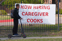 A now hiring sign sits by the sidewalk as a rider on a scooter passes in Garland, Texas, Monday, March 23, 2026. (AP Photo/LM Otero)