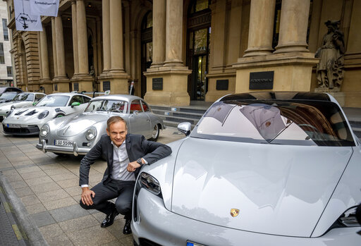 CEO of Porsche car maker Oliver Blume kneels next to Porsche cars at the start of Porsche's market listing at the stock market in Frankfurt, Germany, Thursday, Sept. 29, 2022. (AP Photo/Michael Probst)