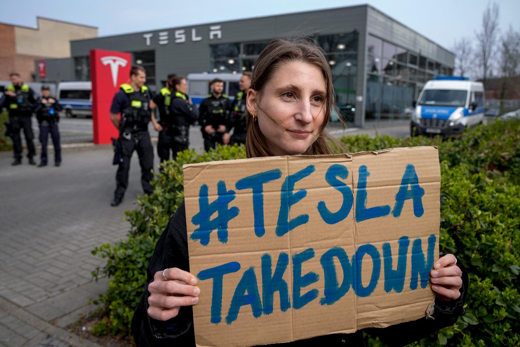 A protester holds a placard during a Tesla Takedown Global Day protest in front of a Tesla dealership, in Berlin, Saturday, March 29, 2025. (AP Photo/Ebrahim Noroozi)