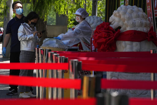 A vendor sells take away food near barriers set up to keep customers spread out on Friday, May 13, 2022, in Beijing. (AP Photo/Ng Han Guan)
