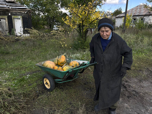 Tatiana, who did not want to give her last name, pulls a hand cart loaded with squashes on the outskirts of the recaptured town of Lyman, Ukraine, Friday, Oct. 7, 2022. Tatiana's home was damaged during a Russian attack while she and her daughter were inside, and she is now rebuilding. She has been wearing the pants and jackets of Russian soldiers, she said, "because all my stuff was destroyed."(AP Photo/Justin Spike)