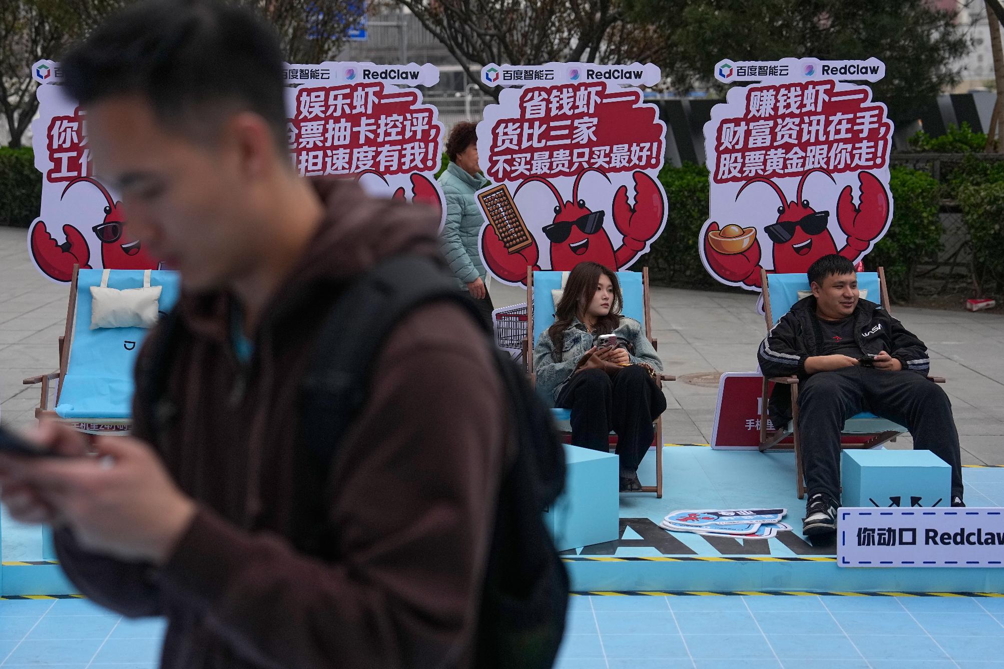 Shoppers rest at a RedClaw AI promotion booth set up outside a shopping mall in Beijing on March 28, 2026. (AP Photo/Andy Wong)