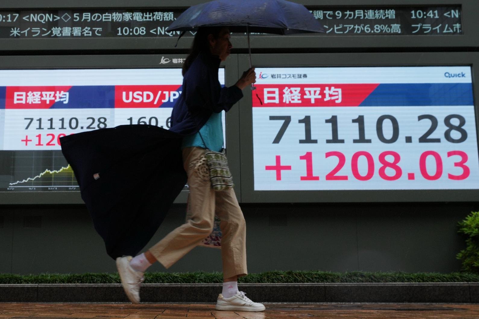 A woman walks past a screen, right, showing Japan's Nikkei 225 index at a securities firm in Tokyo, Thursday, June 18, 2026. (AP Photo/Hiro Komae)