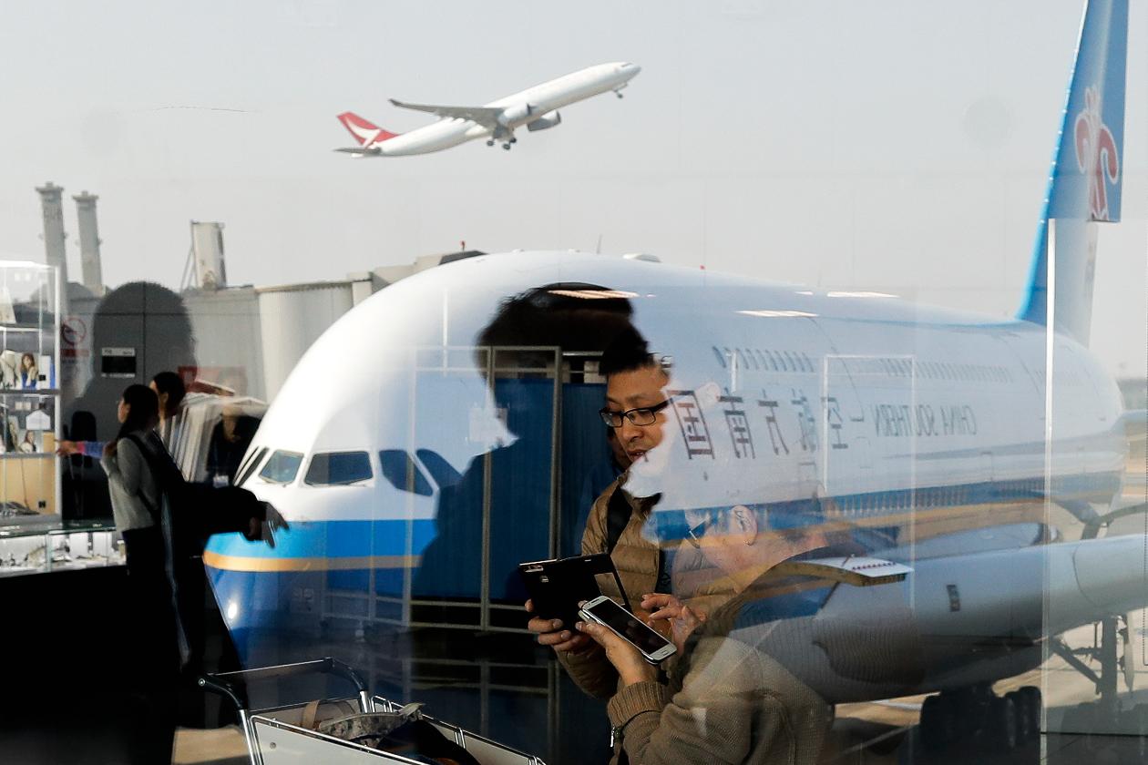 FILE - Passengers walk past a couple browsing their smartphones near a China Southern Airlines, parked on the tarmac at the Beijing Capital International Airport Saturday, Nov. 19, 2016.(AP Photo/Andy Wong, File)
