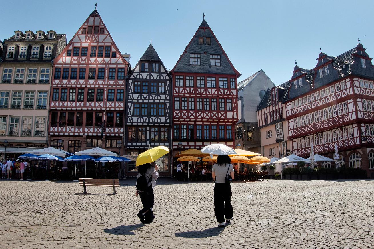 Tourist under umbrellas walk on the Roemerberg square in Frankfurt, Germany, Wednesday, July 2, 2025. (AP Photo/Michael Probst)
