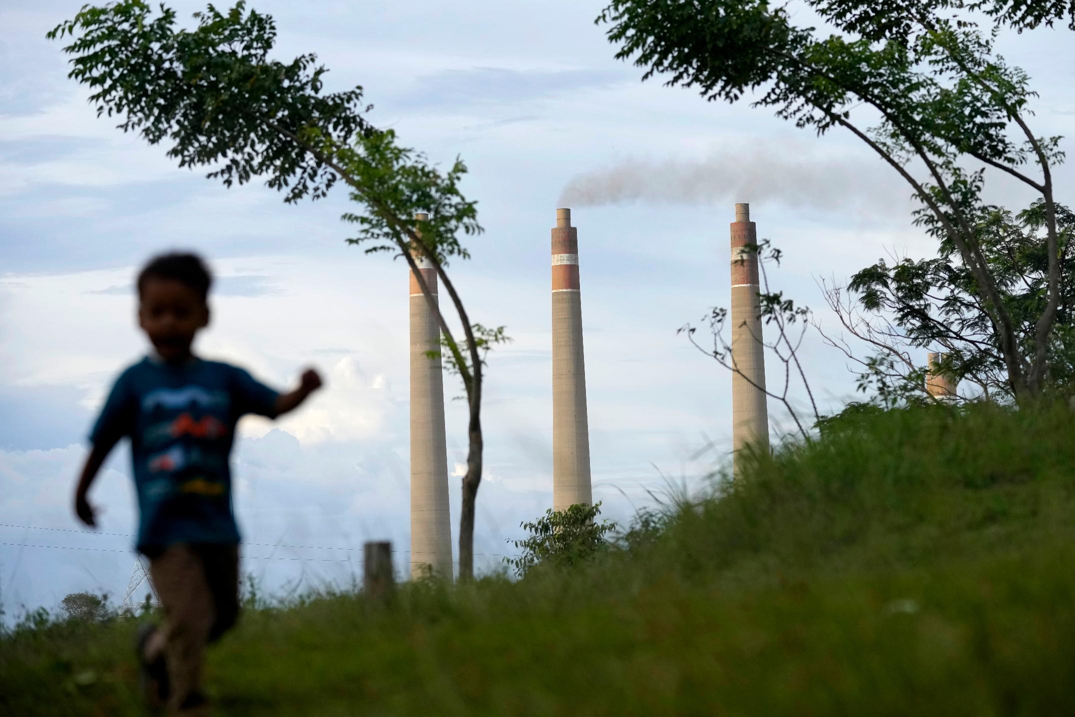 FILE - A young boy plays on a hill called 'Teletubbies Hill', a locally popular tourist attraction, as the chimneys of Suralaya coal power plant loom in the background, in Cilegon, Indonesia, Jan. 8, 2023. (AP Photo/Dita Alangkara, File)