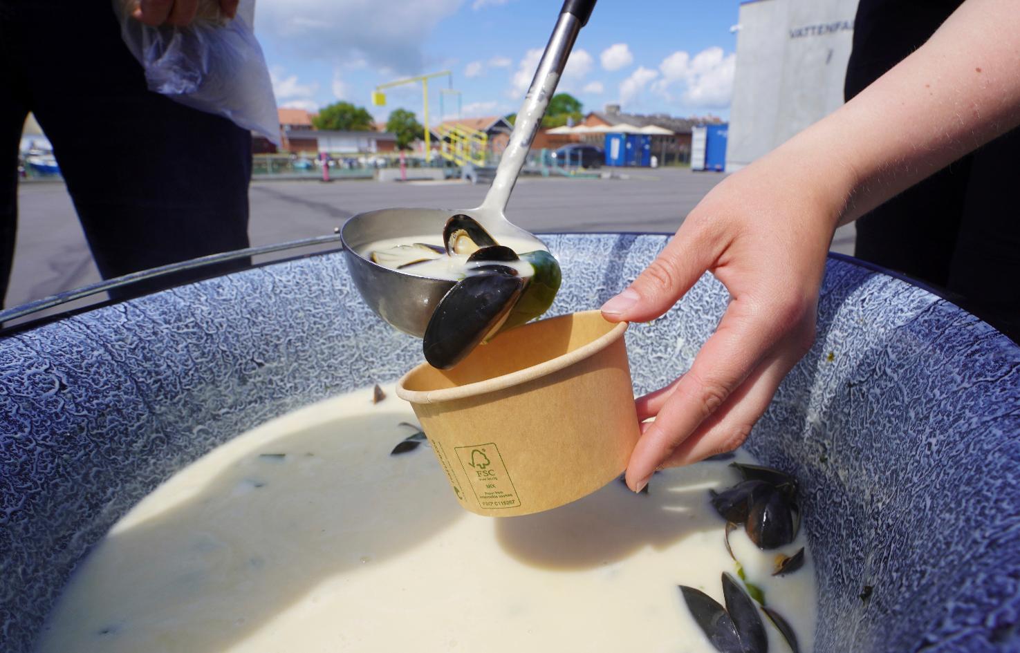 A woman serves mussel soup with seaweed garnish at Klintholm Harbour, Klintholm, Denmark, Tuesday June 18, 2024. (AP Photo/James Brooks)