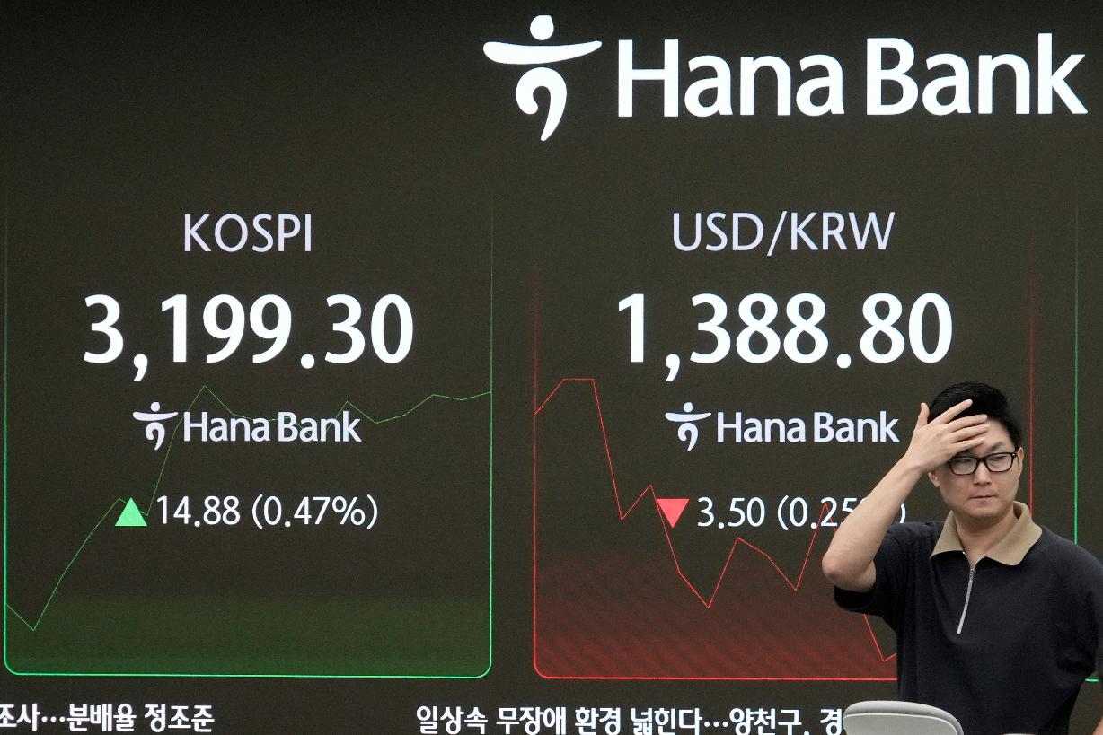 A currency trader passes by a screen showing the Korea Composite Stock Price Index (KOSPI), left, and the foreign exchange rate between U.S. dollar and South Korean won at the foreign exchange dealing room of the Hana Bank headquarters in Seoul, South Korea, Thursday, Sept. 4, 2025. (AP Photo/Ahn Young-joon)