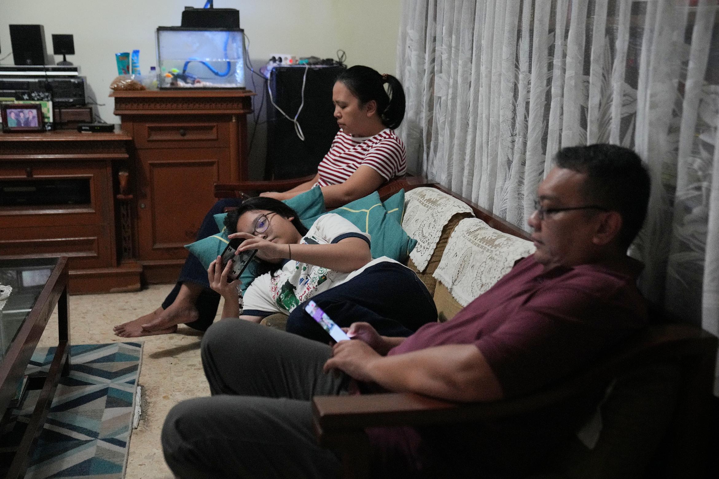 Maura Munthe, center, and her parents Lena Sinuraya, rear, and Ronald, right, use their mobile phone at their house in Jakarta, Indonesia, March 14, 2026. (AP Photo/Dita Alangkara)