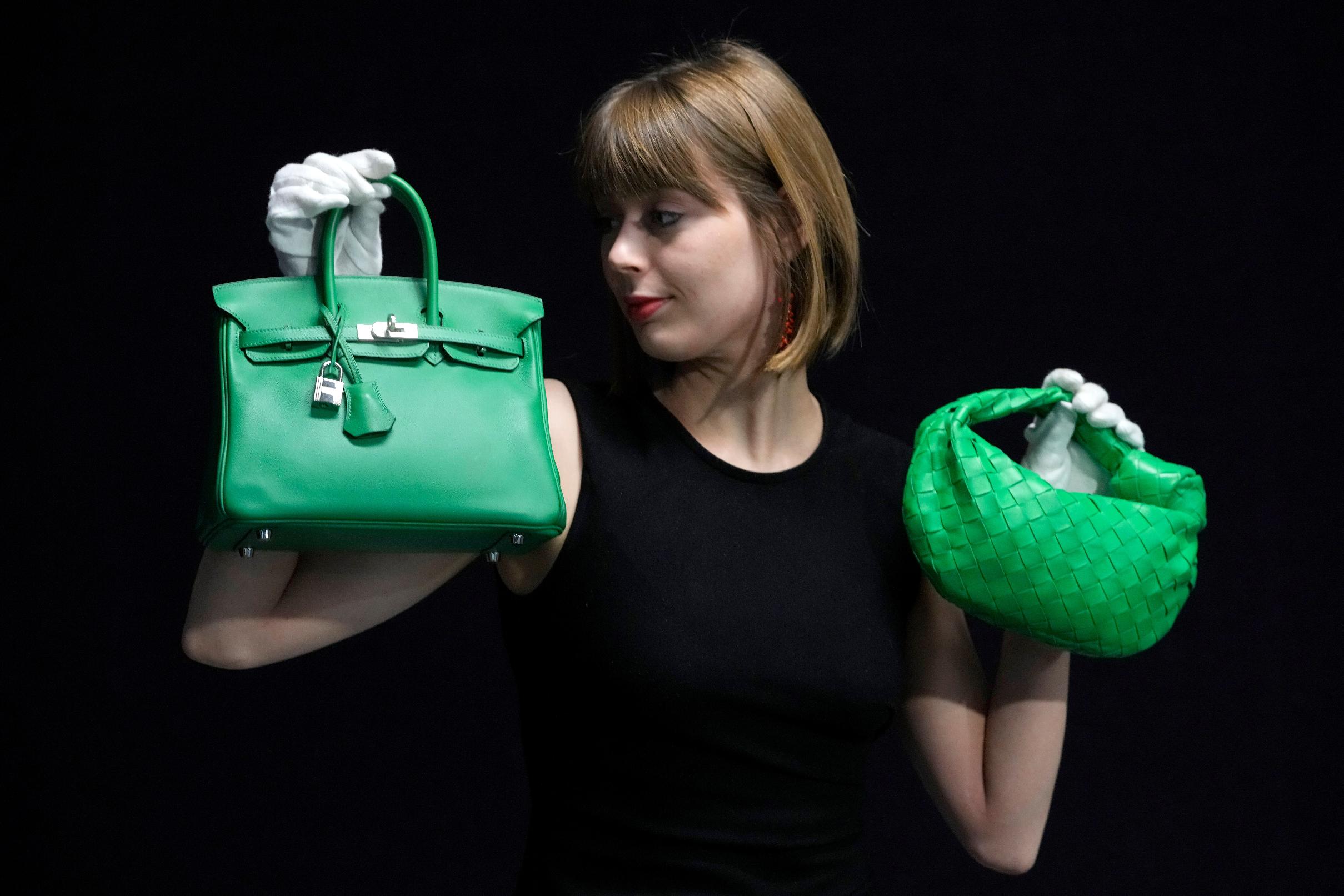 FILE - A Bonhams employee displays a Hermes: a Bambou Swift Leather Birkin 25 bag, left, and a Bottega Veneta: a Parakeet Green Lambskin Mini Jodie, right, at the auction rooms in London on Feb. 26, 2024. (AP Photo/Kirsty Wigglesworth, File)