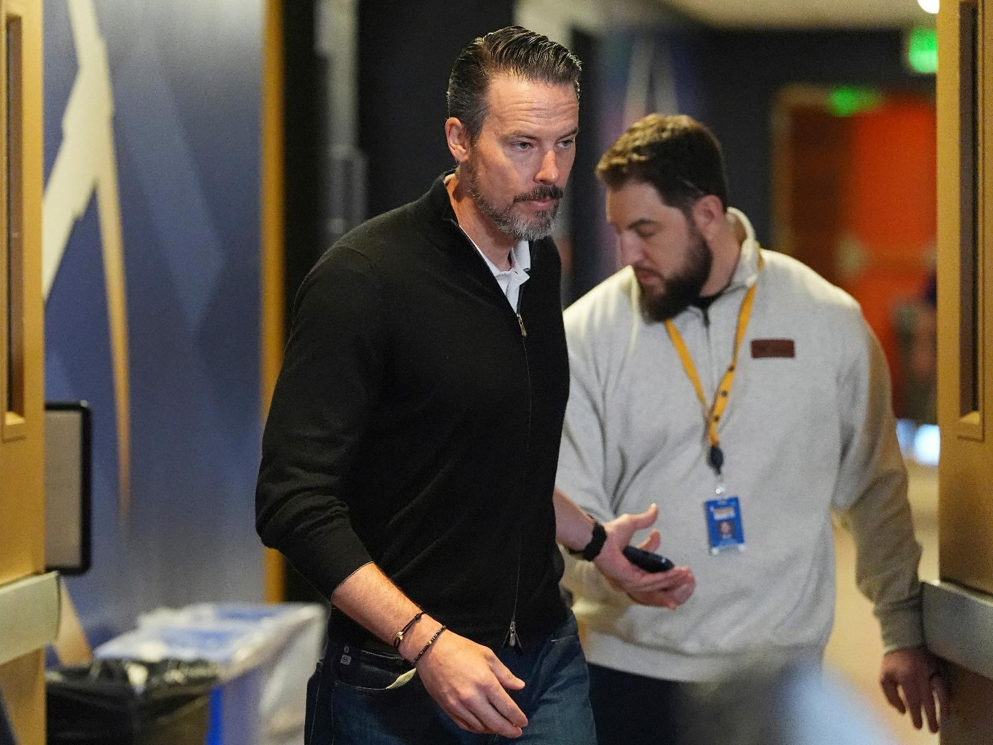 Denver Nuggets team president Josh Kroenke, left, hands off his mobile phone to the Nuggets' media relations manager Nick O'Hayre on the way in to respond at a news conference Monday, April 14, 2025, in Denver to questions about the firing of the team's general manager and head coach last week. (AP Photo/David Zalubowski)