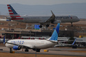An American Airlines jetliner lands on a runway as a United Airlines plane waits for clearance to take off as high winds strafe Denver International Airport Thursday, March 12, 2026, in Denver. (AP Photo/David Zalubowski)