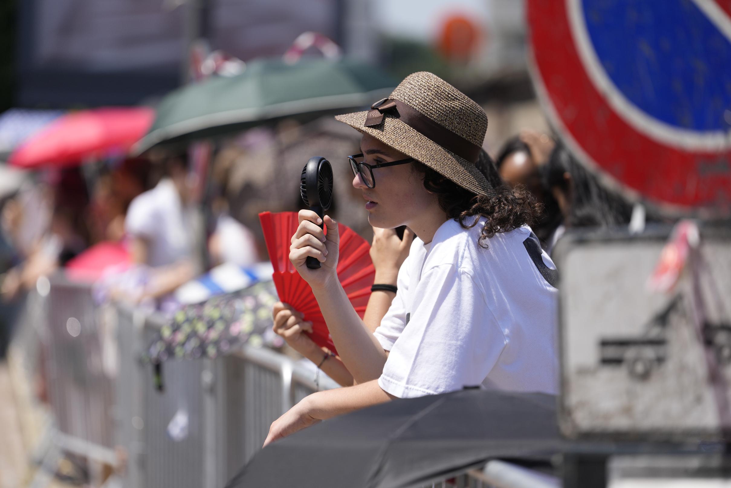 People try to cool off as they wait in the heat the arrival og guests of the Prada's Spring/Summer 2027 men's collection presented in Milan, Italy, Sunday, June 21, 2026. (AP Photo/Luca Bruno)