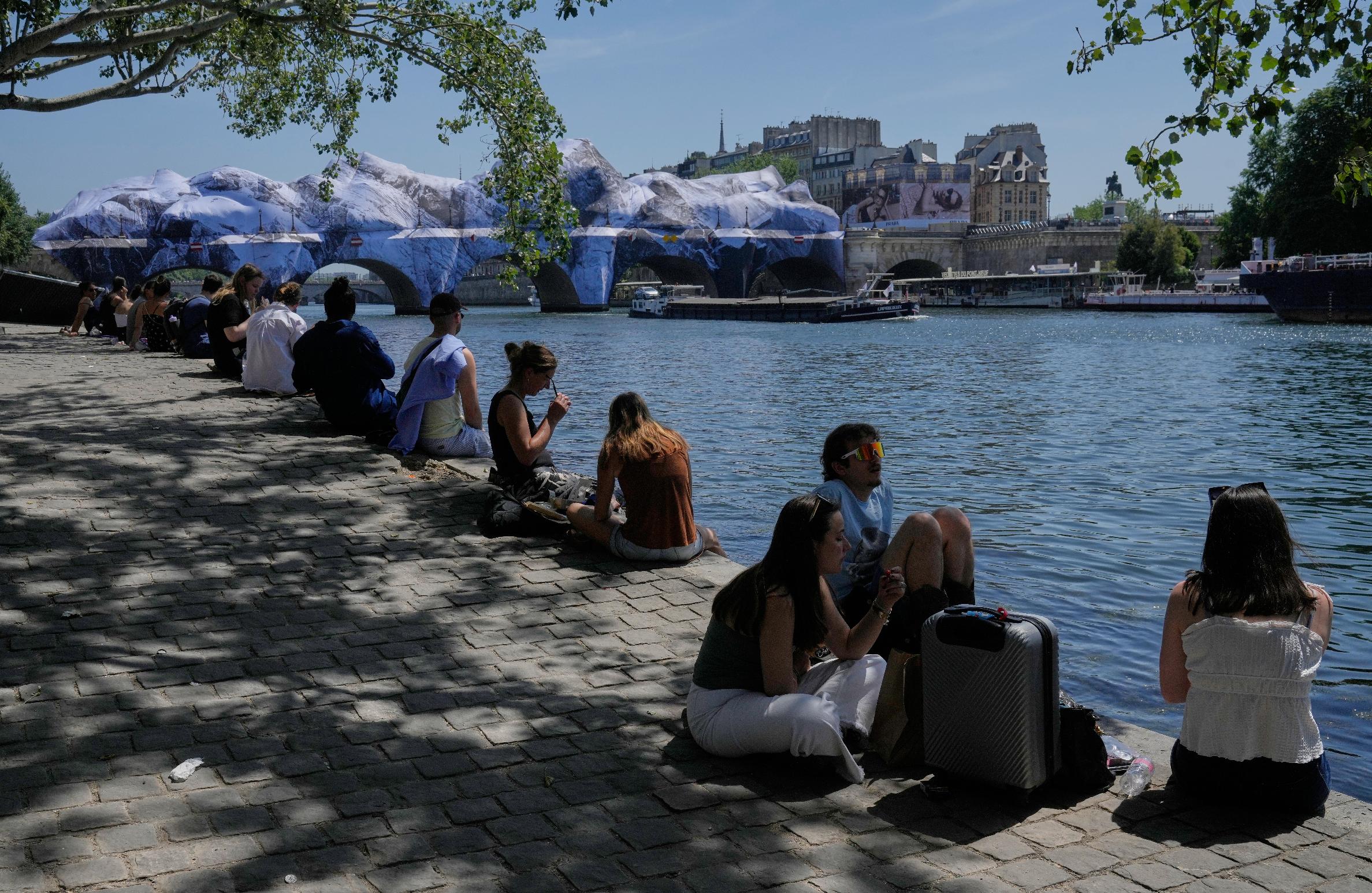 People seek relief from the heat along the Seine River in Paris, Monday, May 25, 2026. Artwork by street artist JR is seen on the Pont Neuf in the background. (AP Photo/Michel Euler)