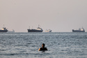 A person stands in shallow water as cargo and commercial vessels are anchored in the Strait of Hormuz off Bandar Abbas, Iran, Monday, June 8, 2026. (Amirhosein Khorgooi/ISNA via AP)