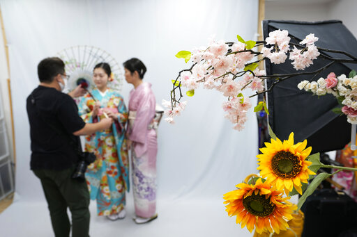 Yusuke Otomo, the owner of Daikichi kimono rental shop, brings a traditional Japanese umbrella for a prop during a photo session of his customers at the shop Wednesday, June 22, 2022, in Tokyo's Asakusa area famous for sightseeing. Japan is bracing for a return of tourists from abroad, as border controls to curb the spread of coronavirus infections are gradually loosened. Otomo can barely contain his excitement. (AP Photo/Hiro Komae)