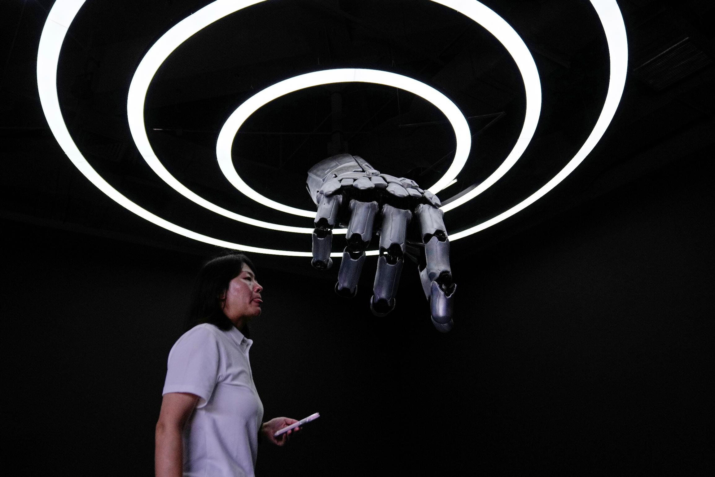 A staff walks in front of robotic arm at the Robot Mall, World's first embodied intelligent robot 4S store in Beijing, China, Wednesday, Aug. 6, 2025. (AP Photo/Mahesh Kumar A.)
