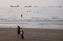 Men walk on the shoreline as people wade in the water in the Strait of Hormuz, where cargo and service vessels are anchored off Bandar Abbas, Iran, Monday, June 1, 2026. (Amirhosein Khorgooi/ISNA via AP)