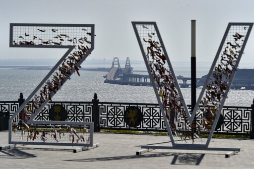 A helicopter dropping water to stop fire on Crimean Bridge connecting Russian mainland and Crimean peninsula over the Kerch Strait, is seen through the letters Z and V, which have become a symbol of the Russian military, in Kerch, Crimea, Saturday, Oct. 8, 2022. Russian authorities say a truck bomb has caused a fire and the collapse of a section of a bridge linking Russia-annexed Crimea with Russia. The bridge is a key supply artery for Moscow's faltering war effort in southern Ukraine. (AP Photo)