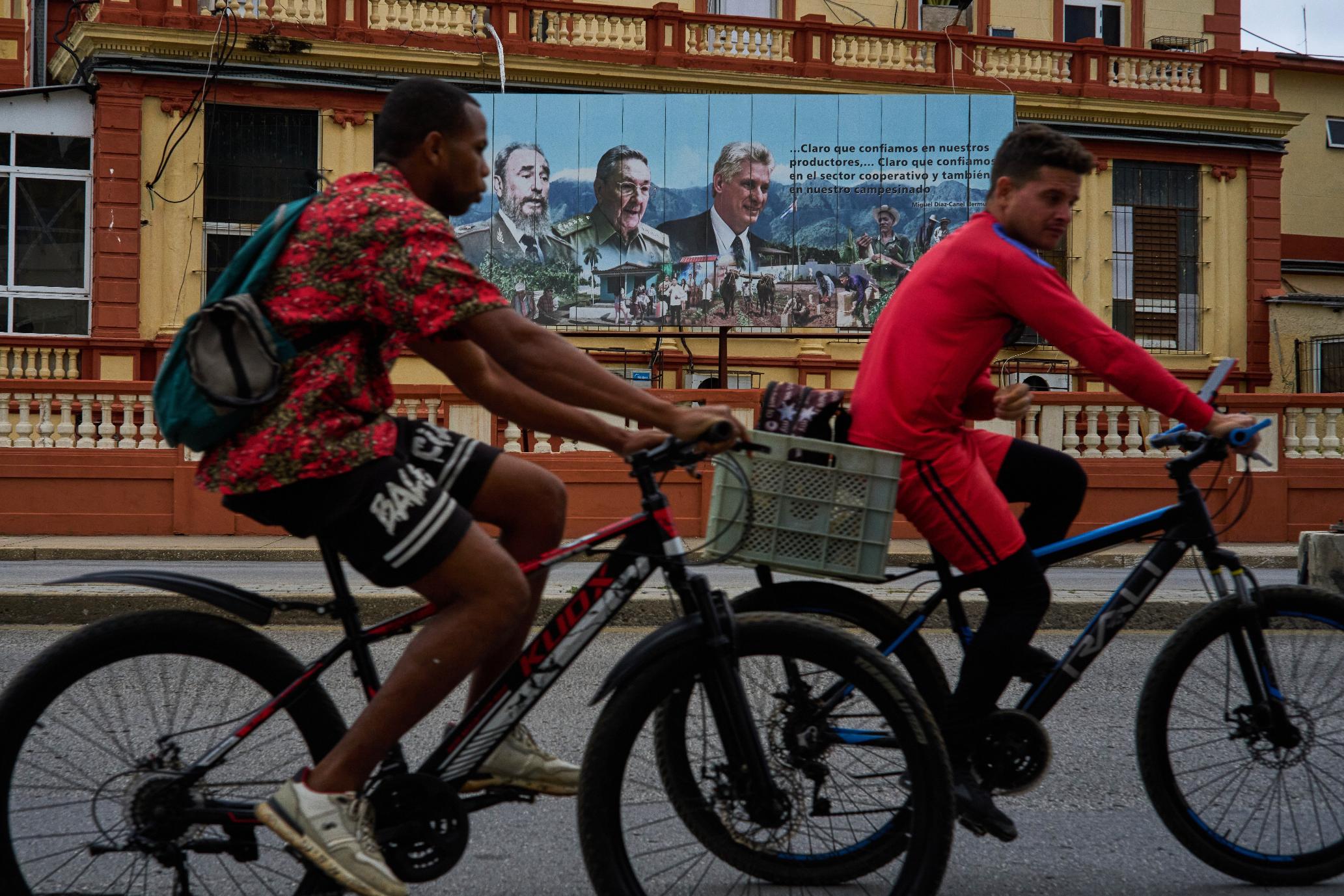 People ride their bicycles in front of images of, from left, past presidents Fidel Castro and Raul Castro, and current President Miguel Diaz-Canel, in Havana, Wednesday, March 18, 2026. (AP Photo/Ramon Espinosa)