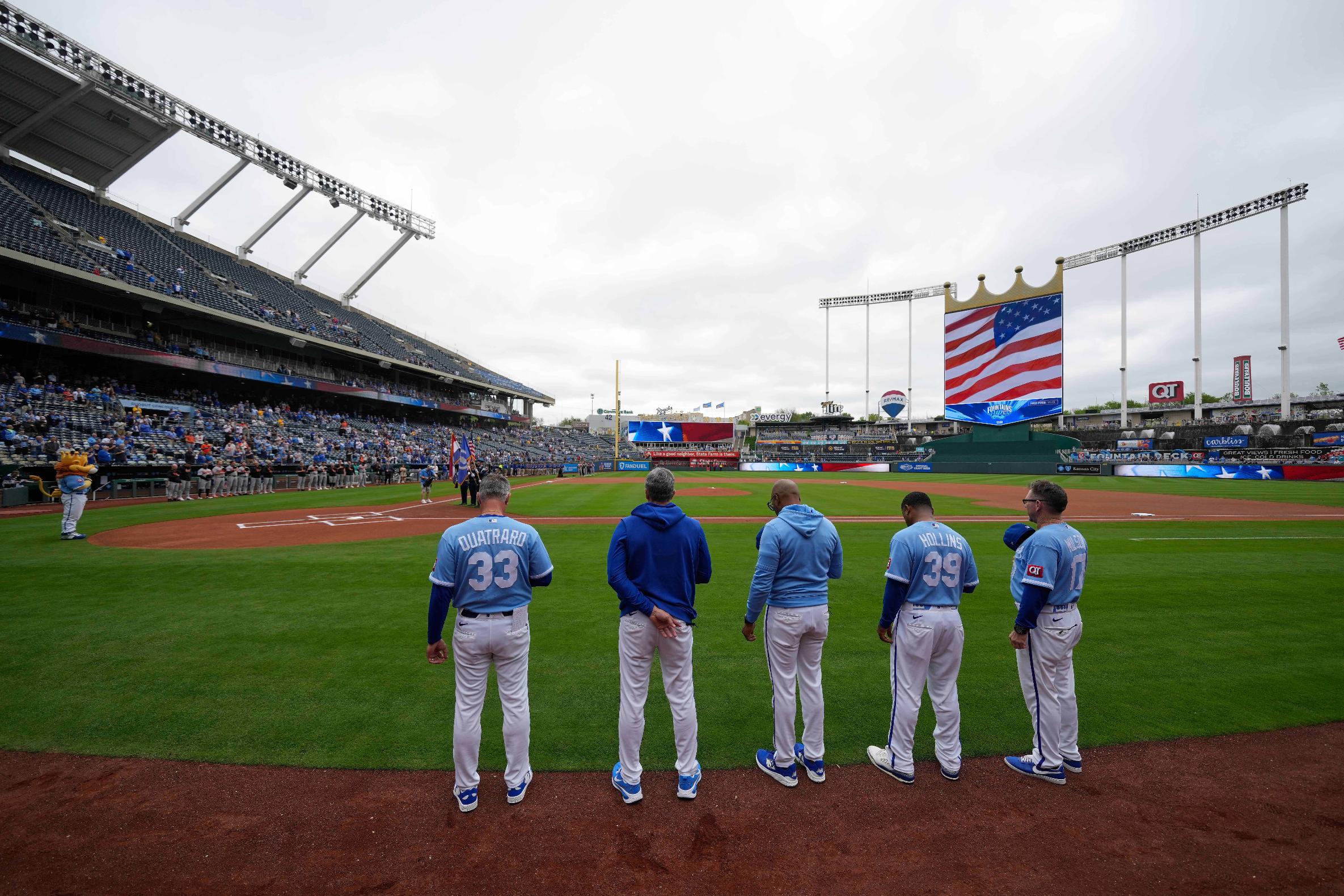Coaches for the Kansas City Royals stand for the national anthem at Kauffman Stadium before a baseball game against the Baltimore Orioles, Wednesday, April 22, 2026, in Kansas City, Mo. (AP Photo/Charlie Riedel)