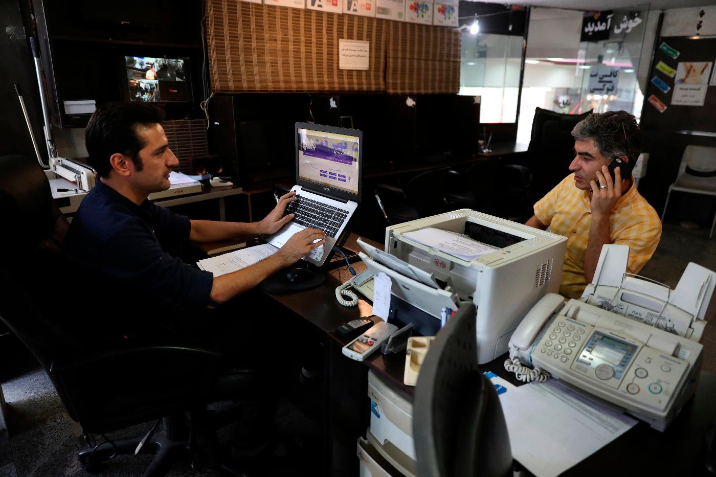 FILE - An internet cafe manager works on his computer as a man talks on his cell phone in Tehran, Iran, July 25, 2019. (AP Photo/Vahid Salemi, File)