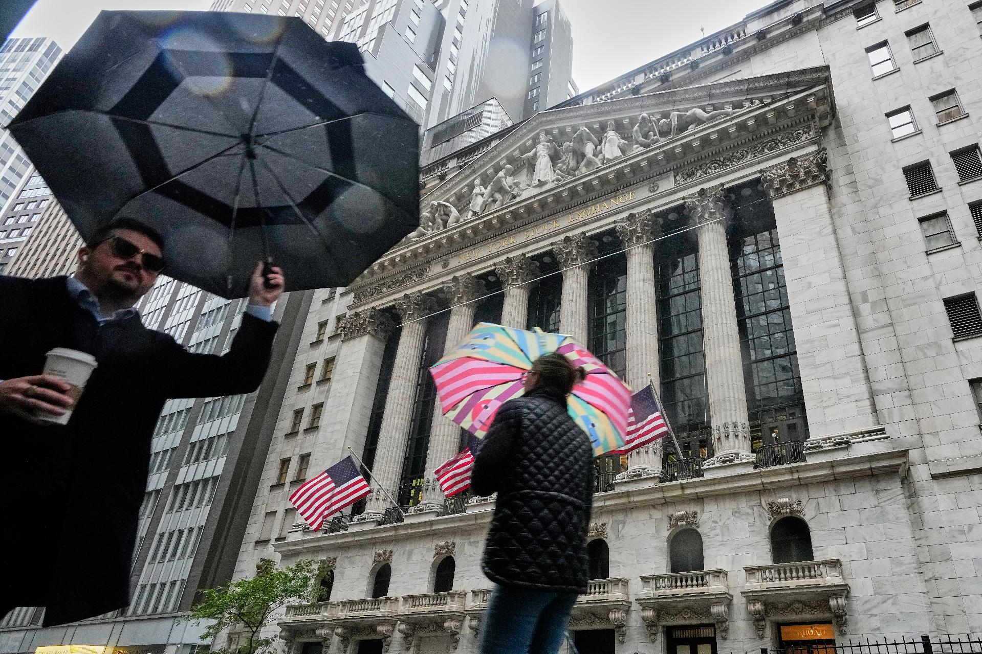 People with umbrellas pass the New York Stock Exchange, Monday, Oct. 13, 2025. (AP Photo/Richard Drew)