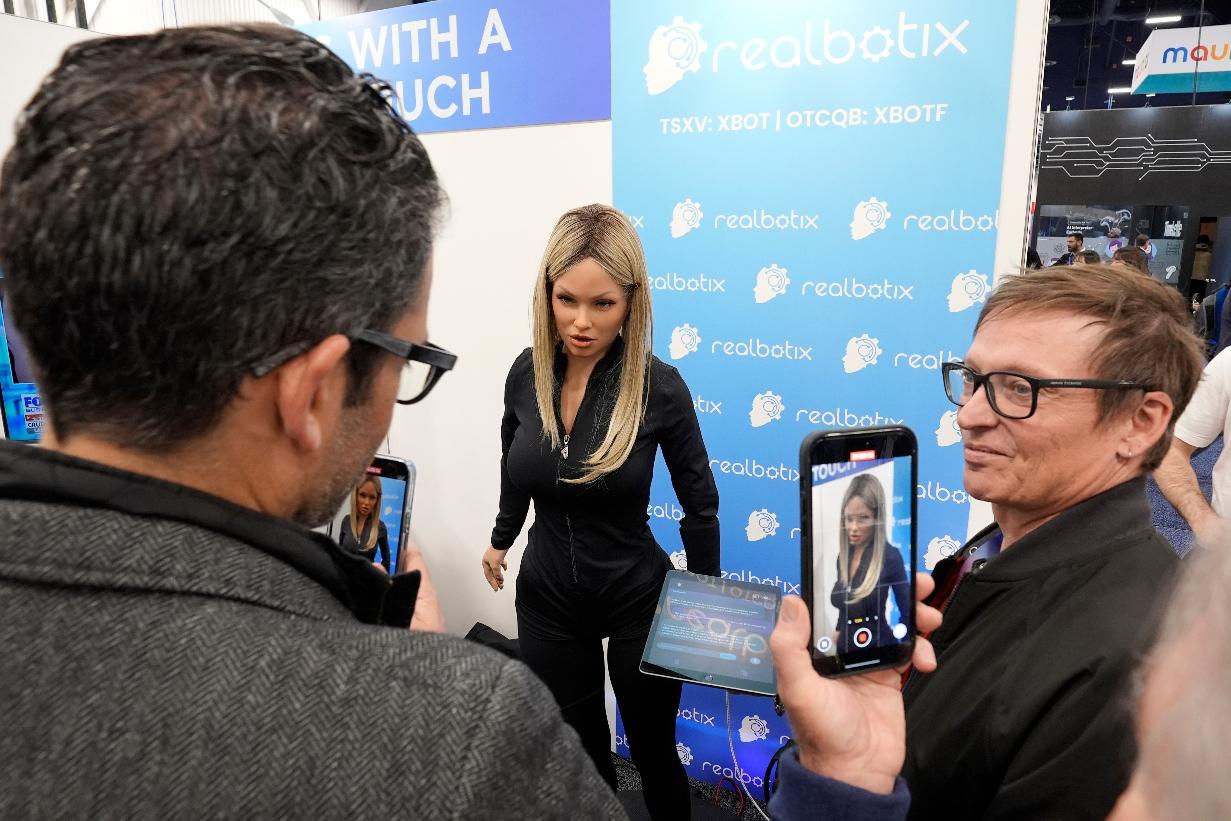 FILE - A Realbotix humanoid robot, center, speaks with attendees at a Realbotix booth during the CES tech show Jan. 8, 2025, in Las Vegas. (AP Photo/Abbie Parr, File)
