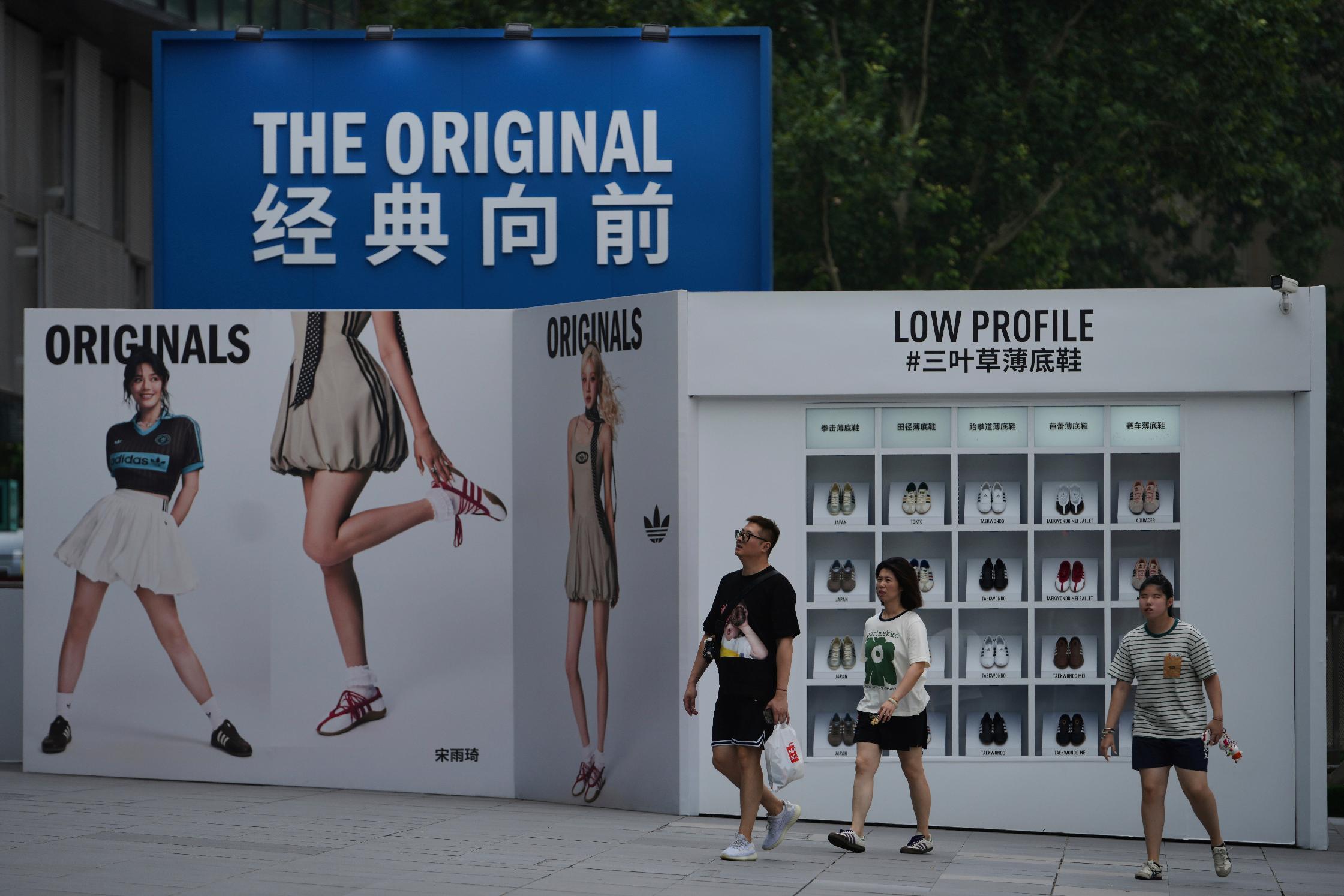 People walk by an Adidas advertisement billboard promoting it latest shoes on display outside a shopping mall, in Beijing, Monday, Aug 4, 2025. (AP Photo/Andy Wong)