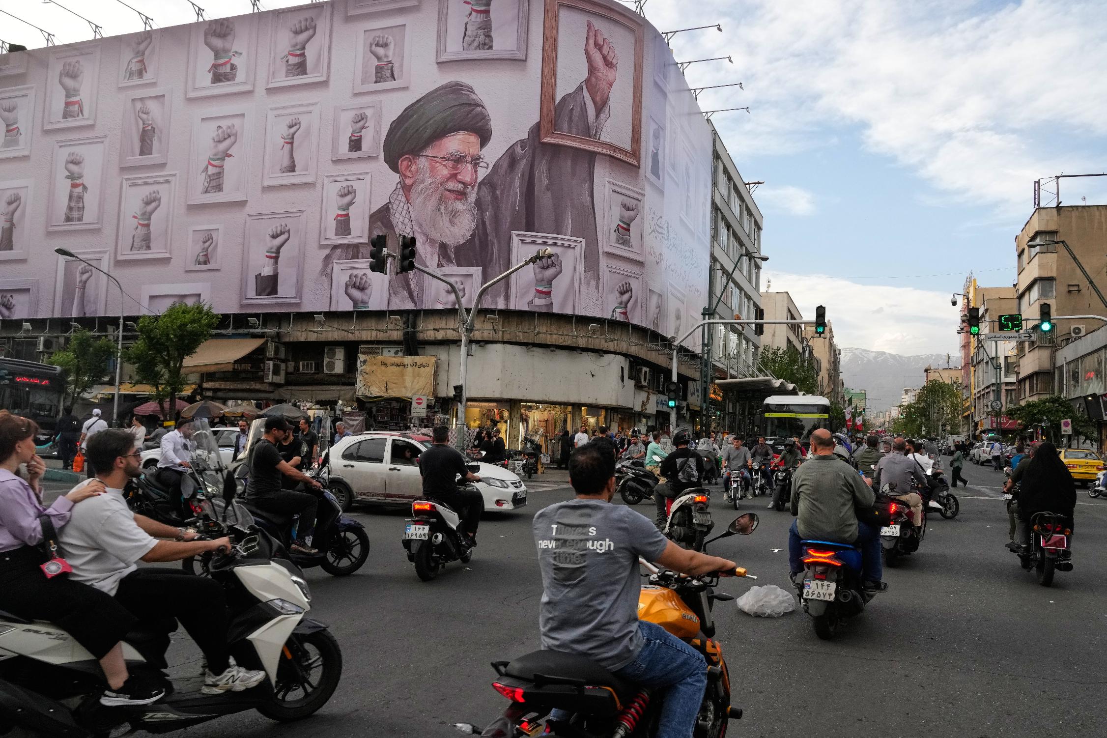Motorbikes drive past a billboard with graphic showing the late Iranian Supreme Leader Ayatollah Ali Khamenei, who was killed in the U.S. and Israel strikes on Feb. 28, with his framed fist amongst his supporters framed fists in downtown Tehran, Iran, Wednesday, May 6, 2026. (AP Photo/Vahid Salemi)