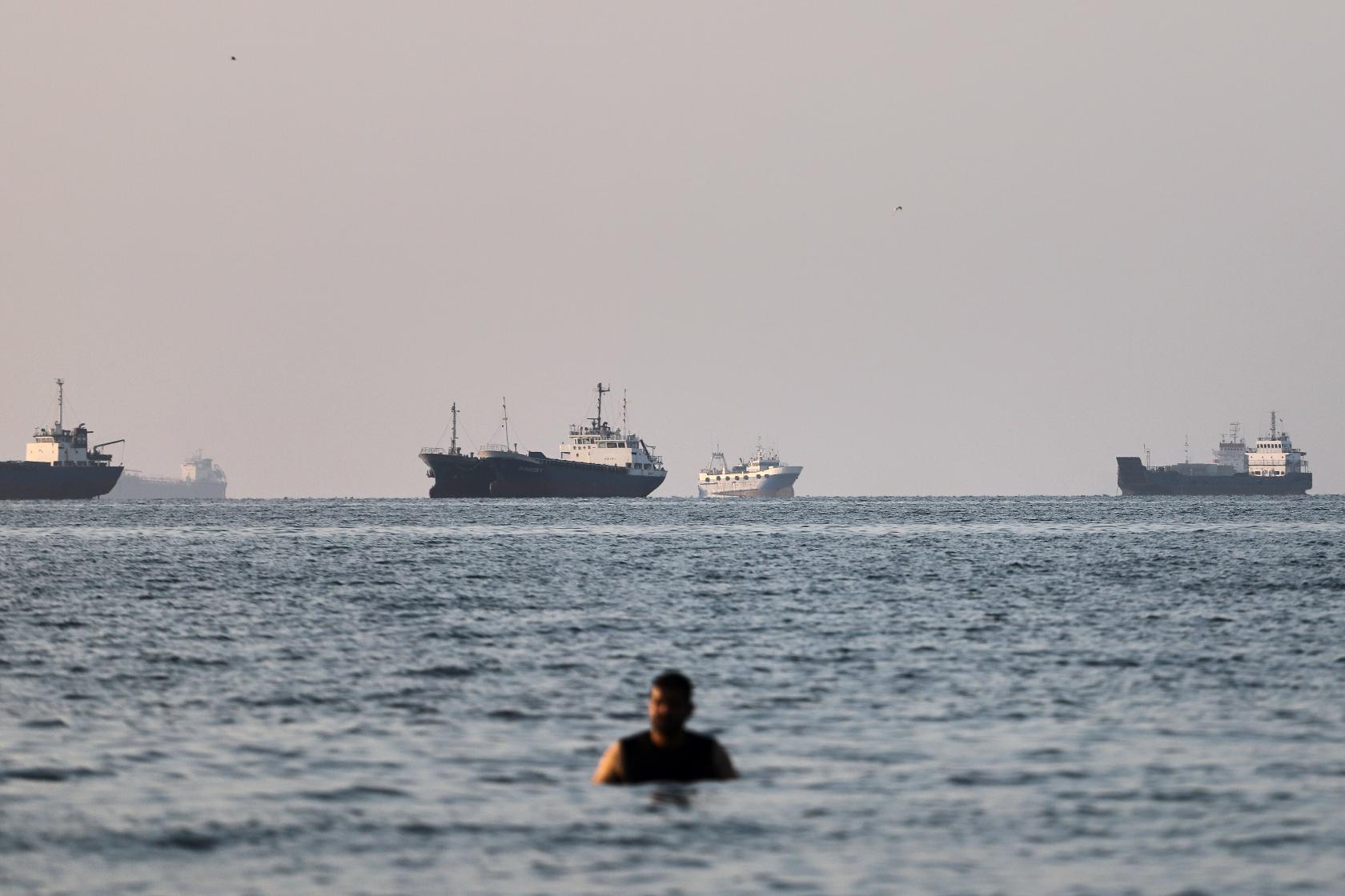 A person stands in shallow water as cargo and commercial vessels are anchored in the Strait of Hormuz off Bandar Abbas, Iran, Monday, June 8, 2026. (Amirhosein Khorgooi/ISNA via AP)