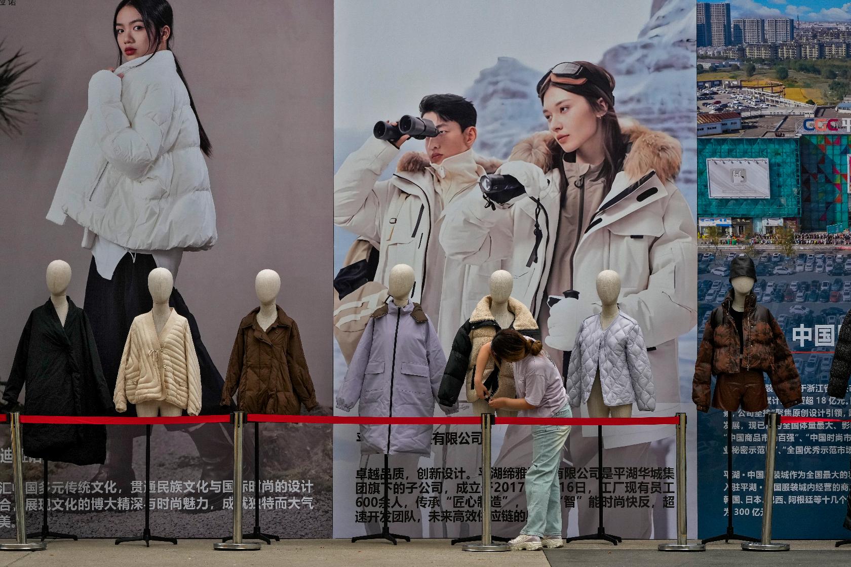 A woman sets up mannequins displaying winter clothes near a booth promoting China made clothing in Beijing on Tuesday, Sept. 10, 2024. (AP Photo/Andy Wong)