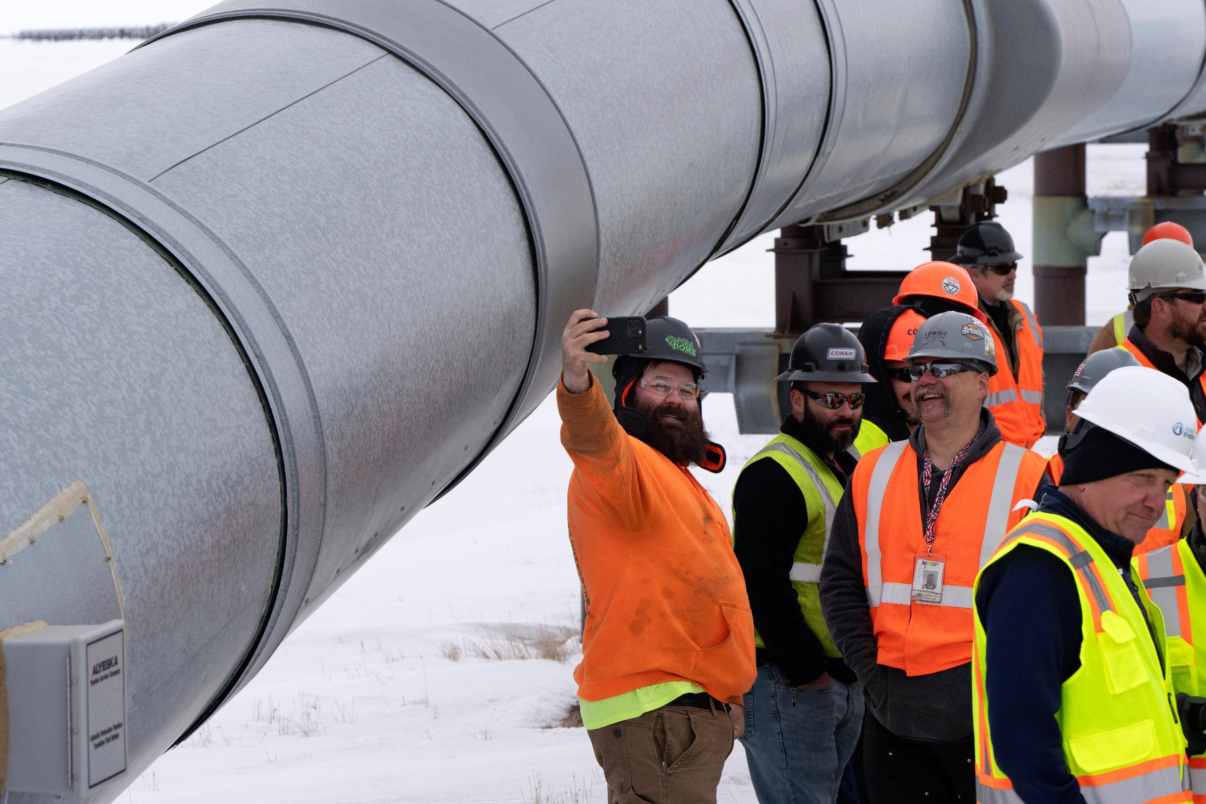A worker poses for a photo with start of the Trans-Alaska Pipeline in the background after a news conference at the Pump Station 1 on Monday, June 2, 2025, located near Deadhorse, Alaska, on the state's prodigious North Slope. (AP Photo/Jenny Kane)
