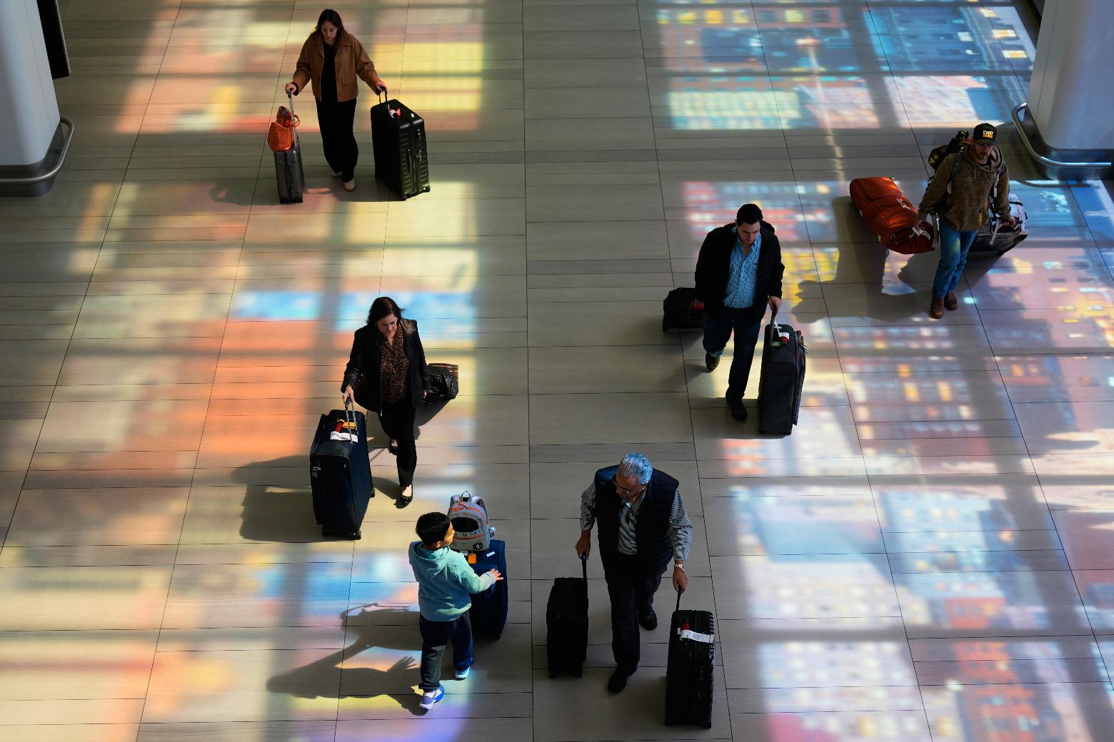 Stained-glass windows cast colorful shadows on the floor as travelers walk through LaGuardia Airport in New York, Monday, March 30, 2026. (AP Photo/Seth Wenig)