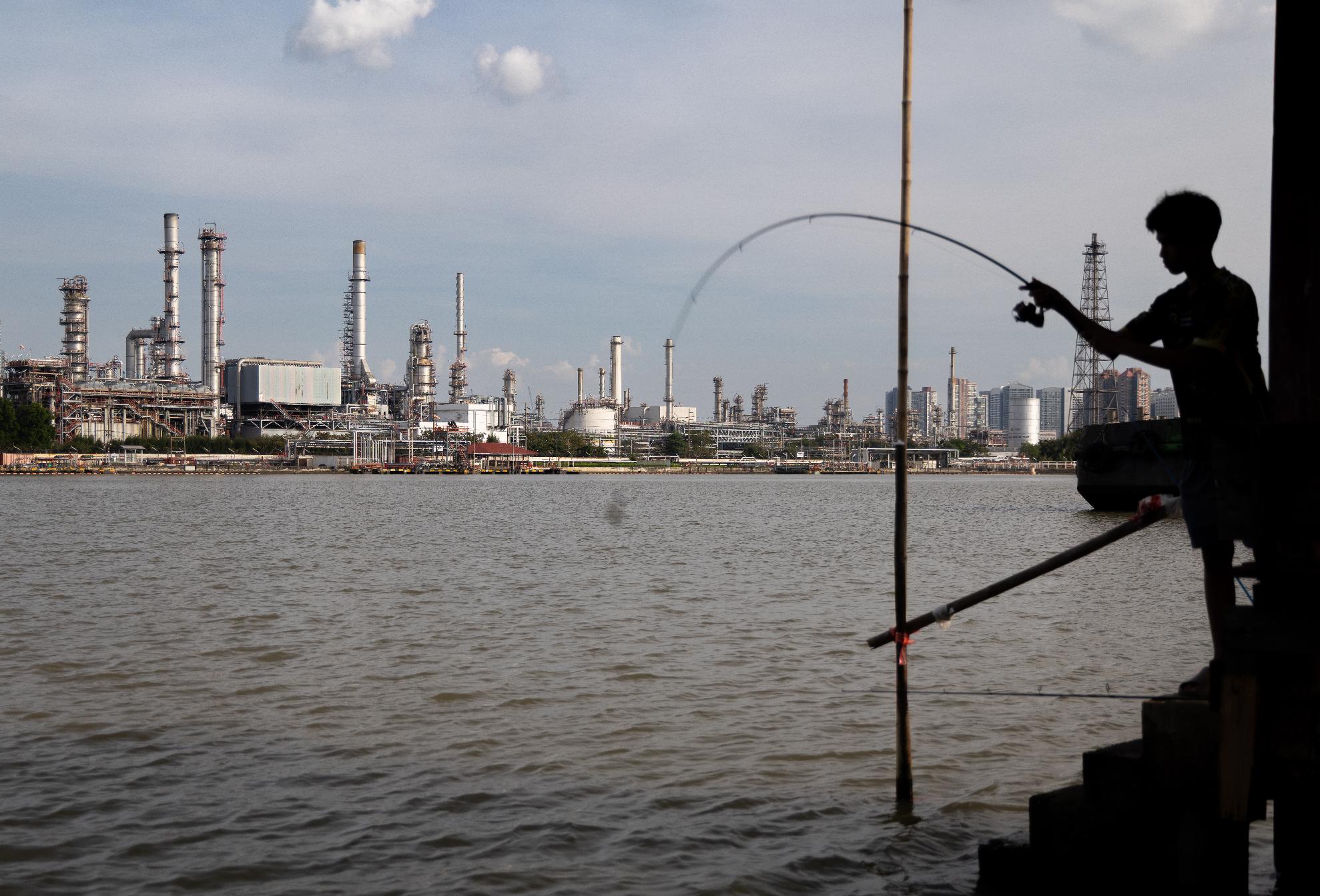 A boy fishes in front of the Bangchak Oil Refinery, home to Thailand's newest sustainable aviation fuel facility, in Bangkok on Jan. 3, 2026. (AP Photo/Anton L. Delgado)