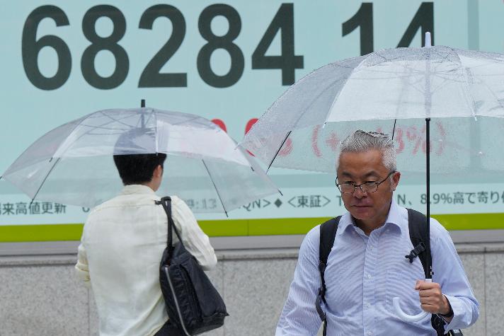 People walk in the rain near electronic stock board showing Japan's Nikkei index at a securities firm Thursday, Aug. 13, 2026, in Tokyo. (AP Photo/Eugene Hoshiko)