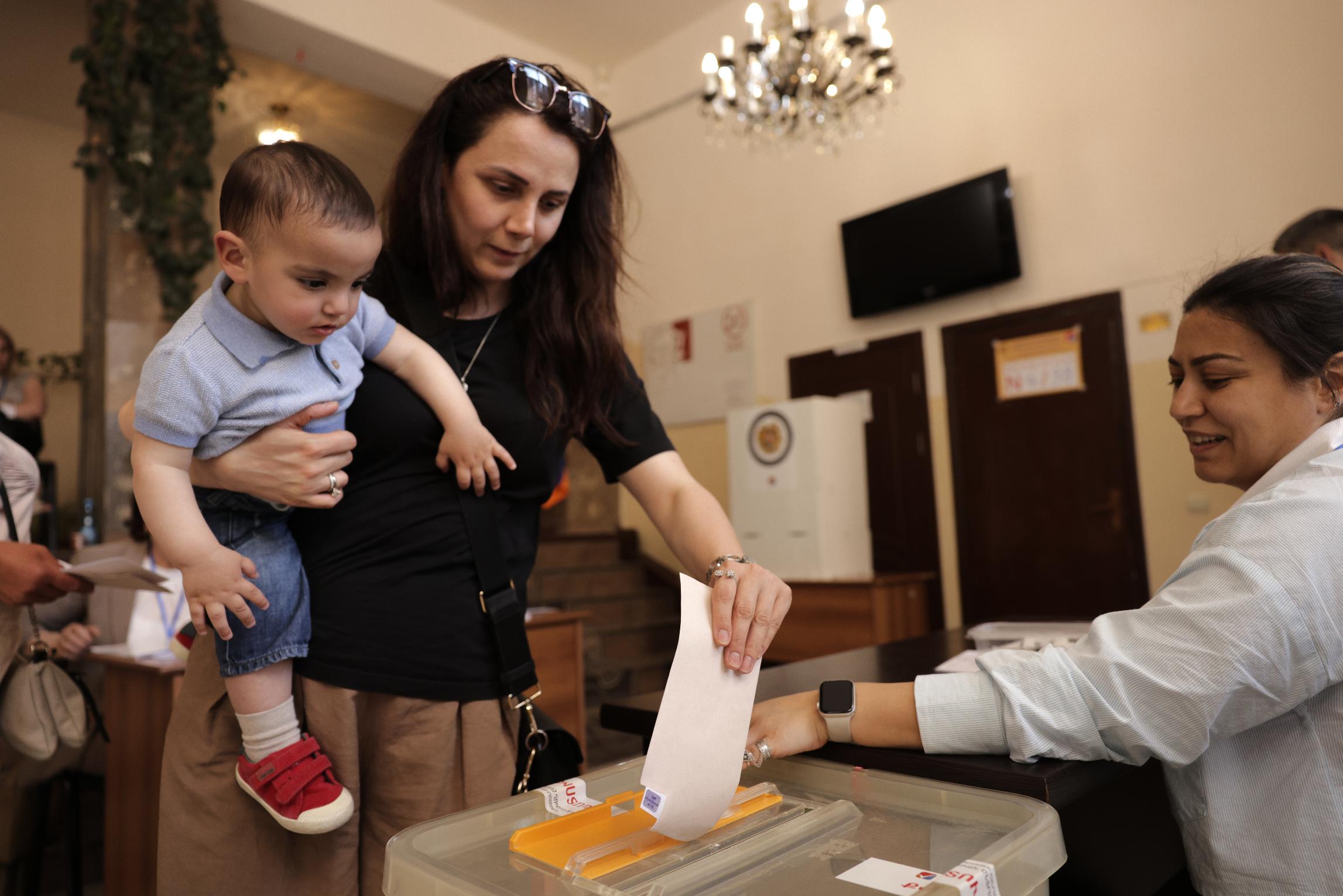 A woman holding a child casts her ballot at a polling station during a parliamentary election in Yerevan, Armenia, Sunday, June 7, 2026. (AP Photo/Anthony Pizzoferrato)