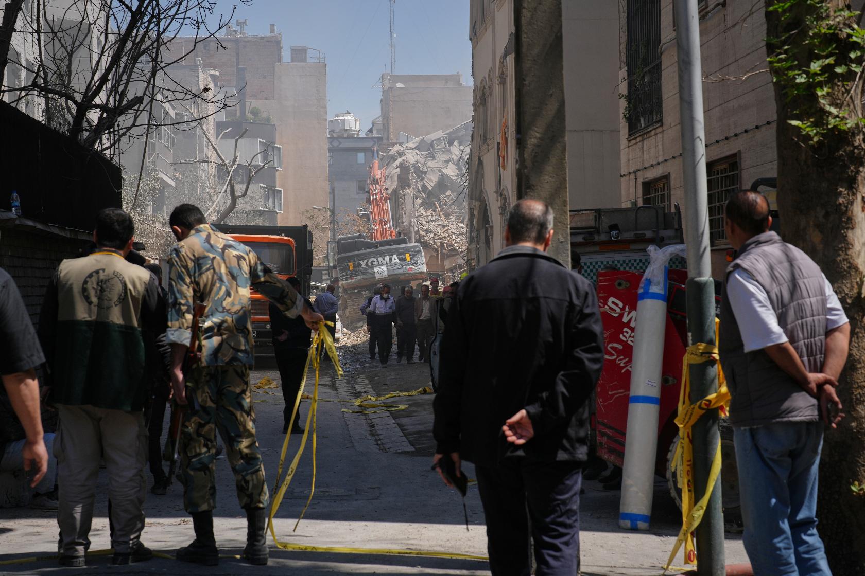 Bystanders watch from a distance as rescue teams and first responders work at the site of a strike that, according to a security official at the scene, destroyed half of the Khorasaniha Synagogue and nearby residential buildings in Tehran, Iran, Tuesday, April 7, 2026. (AP Photo/Francisco Seco)